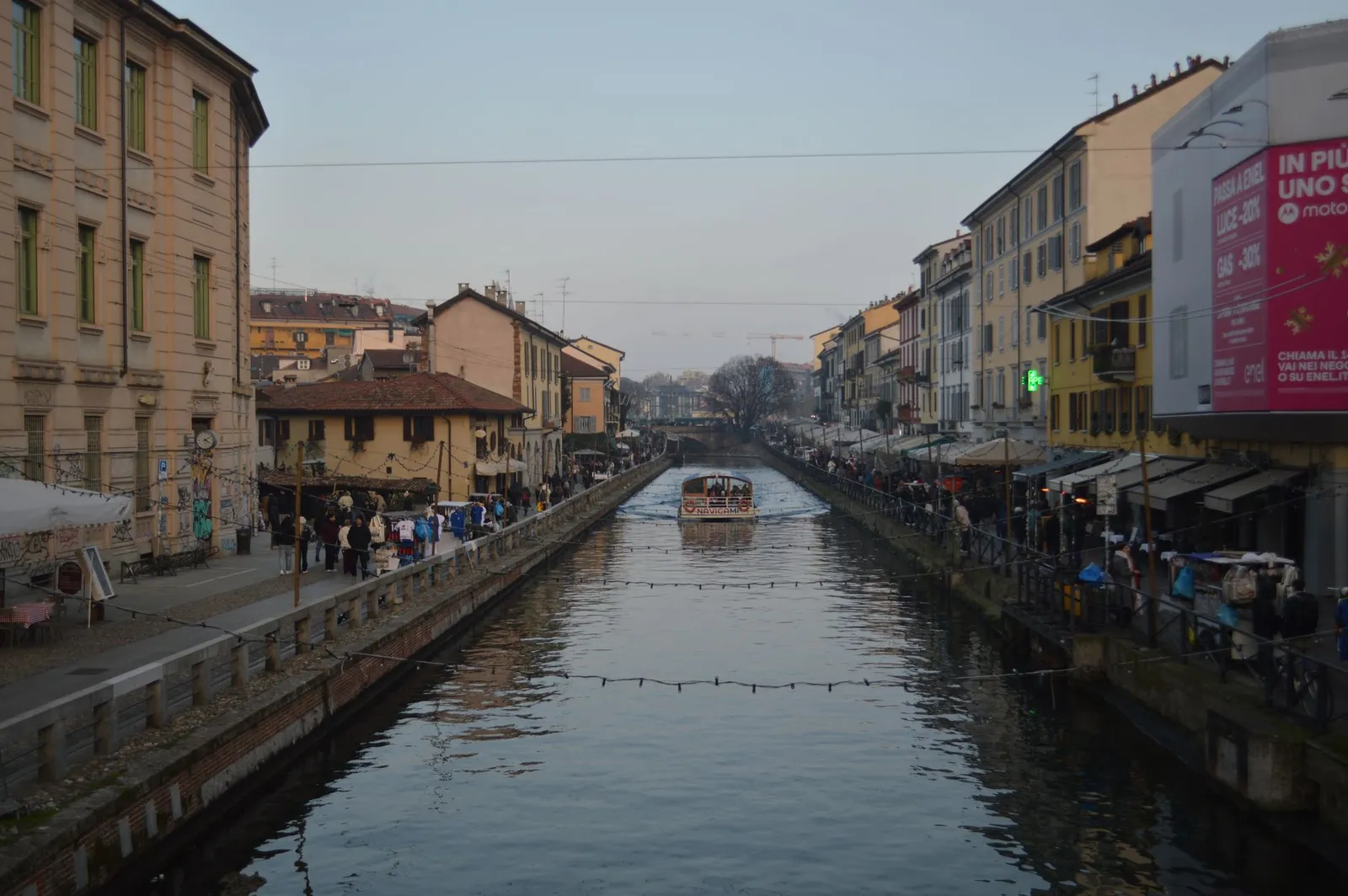 A picturesque canal with bustling streets in Milan's Navigli, showcasing vibrant city life at dusk.