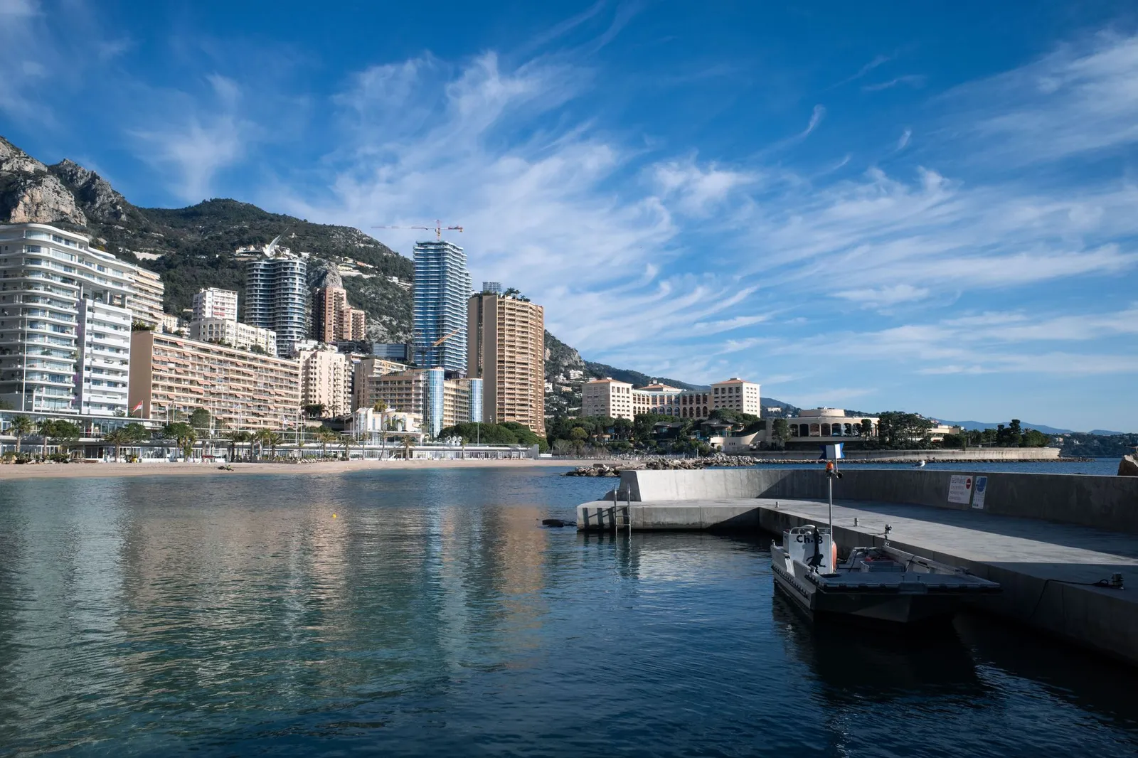 Explore Monaco's stunning waterfront with skyscrapers, mountains, and a clear blue sky.