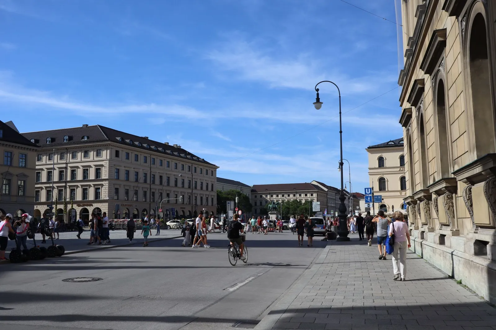 Odeonsplatz in Munich with people walking and cycling under a clear blue sky.