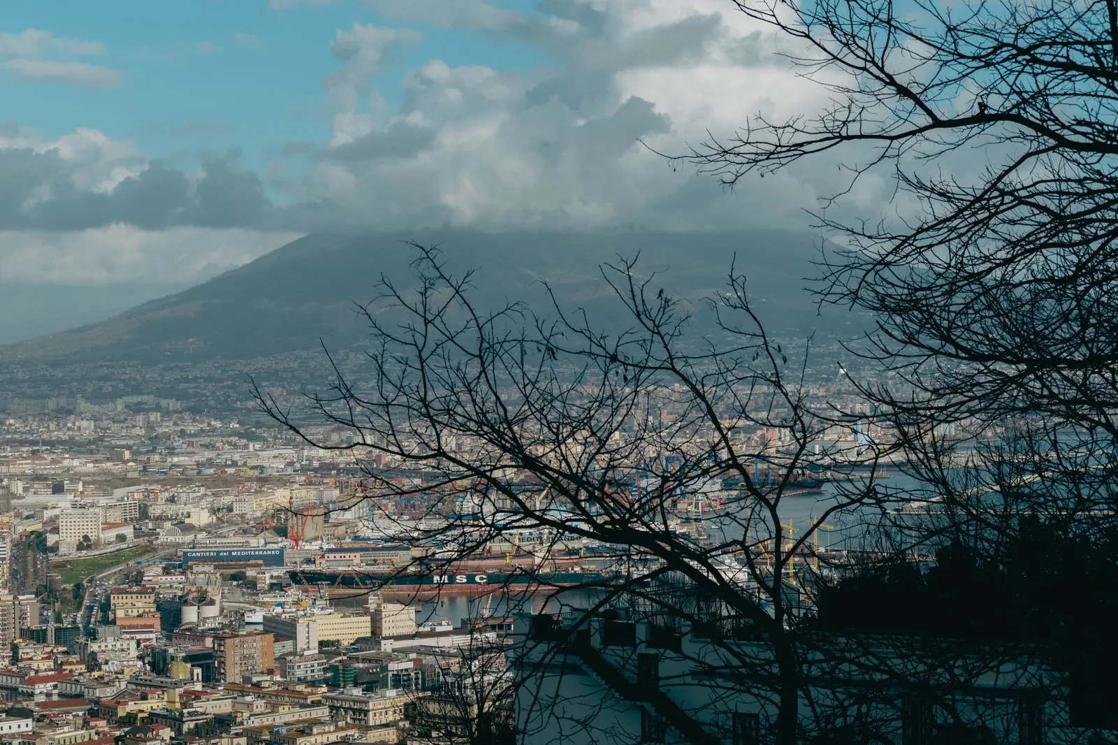 A panoramic view of Naples, Italy with Mount Vesuvius in the background, captured during the day.
