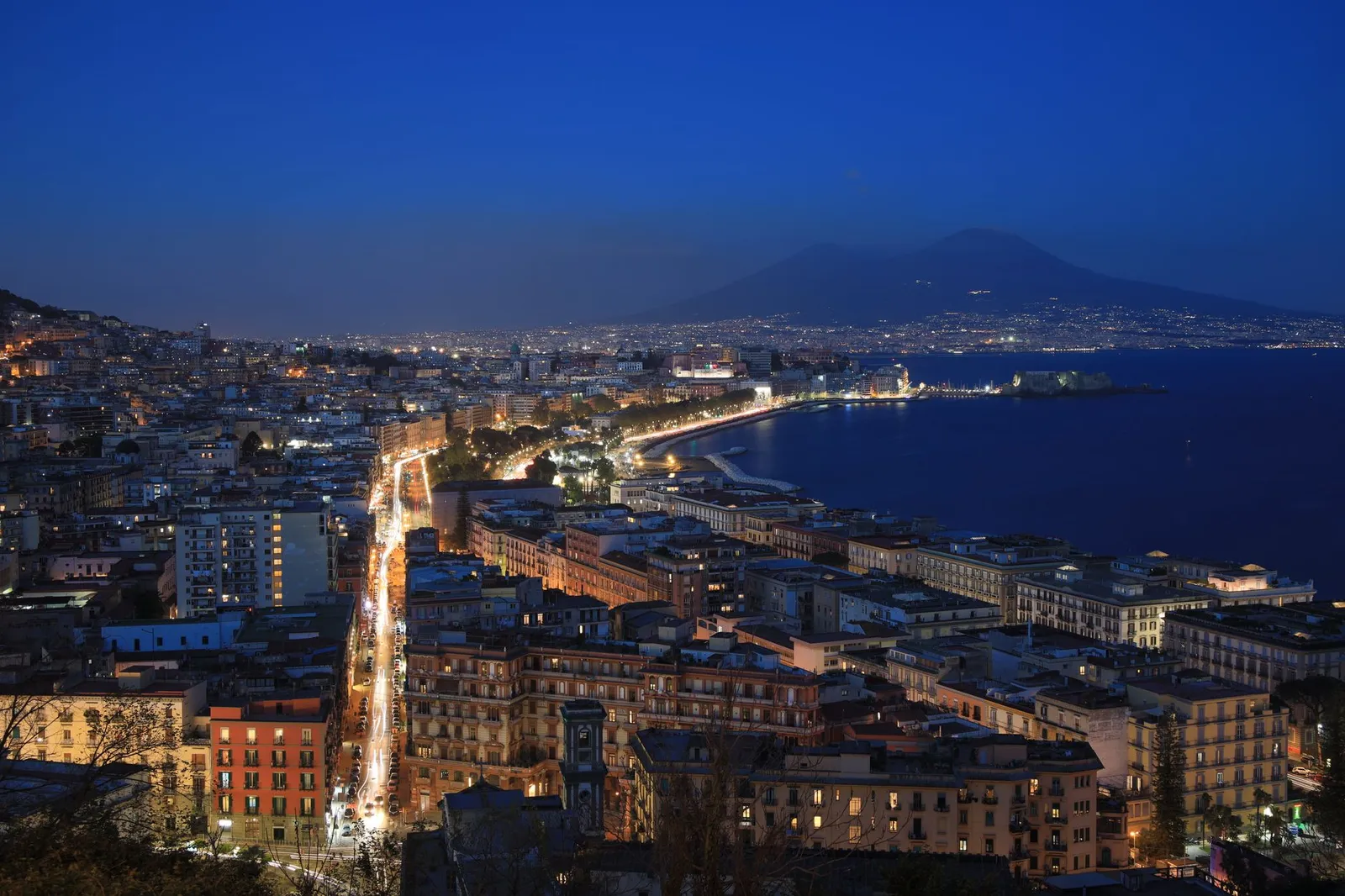 A breathtaking aerial view of Naples cityscape and Mount Vesuvius under evening lights.