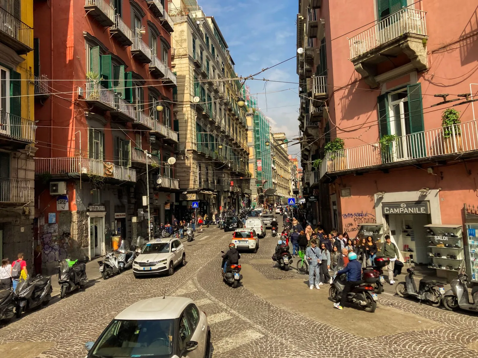 Bustling city street in Naples, Italy with scooters and pedestrians on a sunny day.