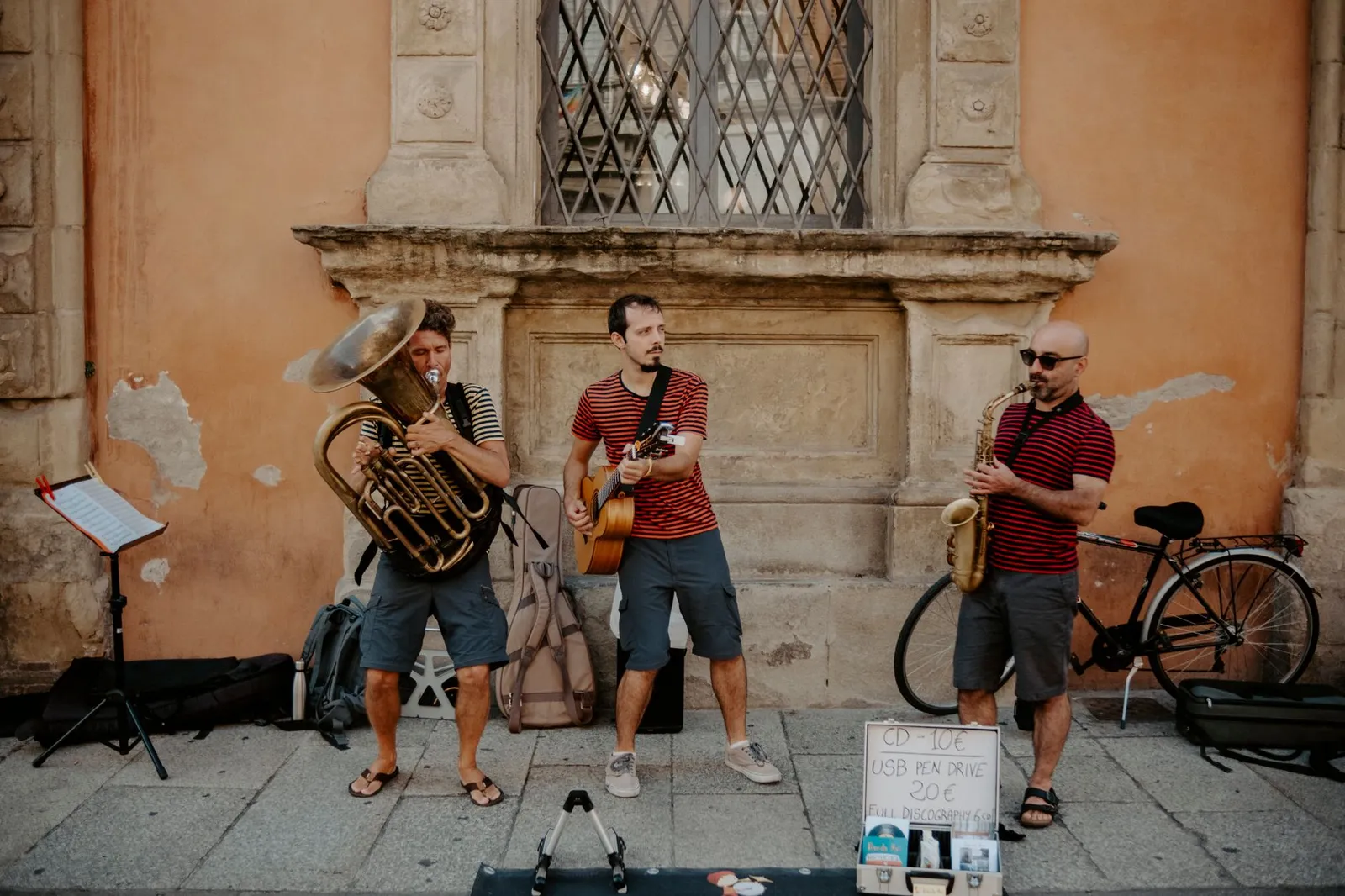 Three musicians busking with tuba, guitar, and saxophone on a city street.