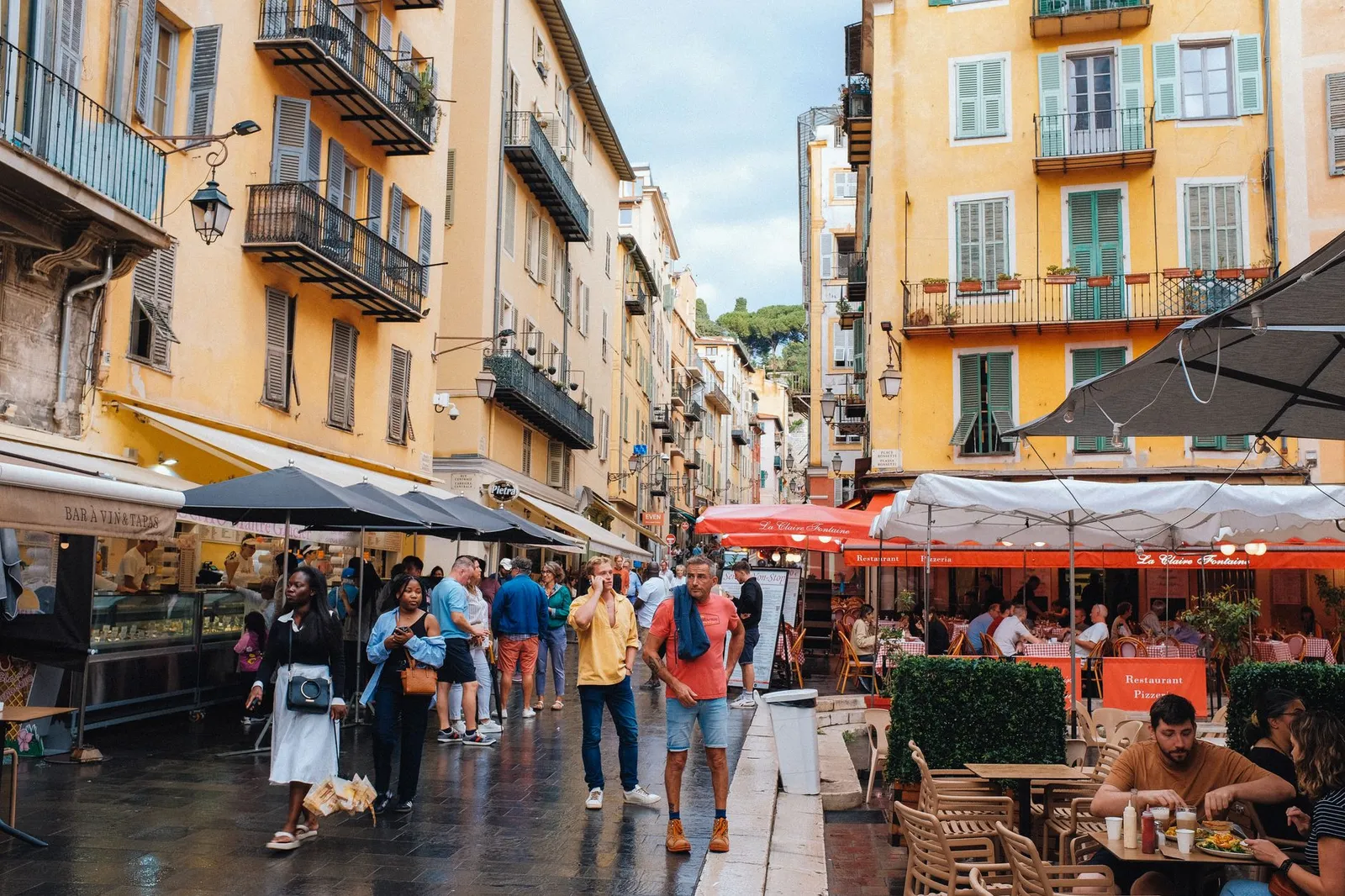 Bustling street in Nice, France with colorful buildings, cafes, and diverse crowd.