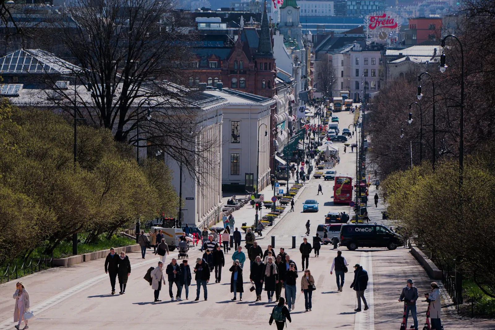 Crowd of people walking along Karl Johans Gate, Oslo on a sunny day with city backdrop.