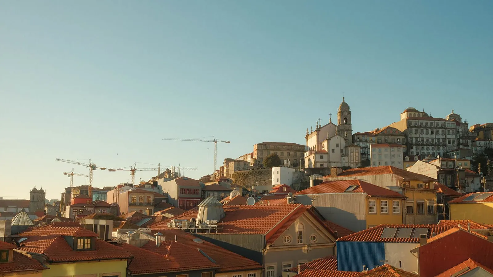 Panoramic view of Porto, Portugal with historic rooftops and cranes at sunset.