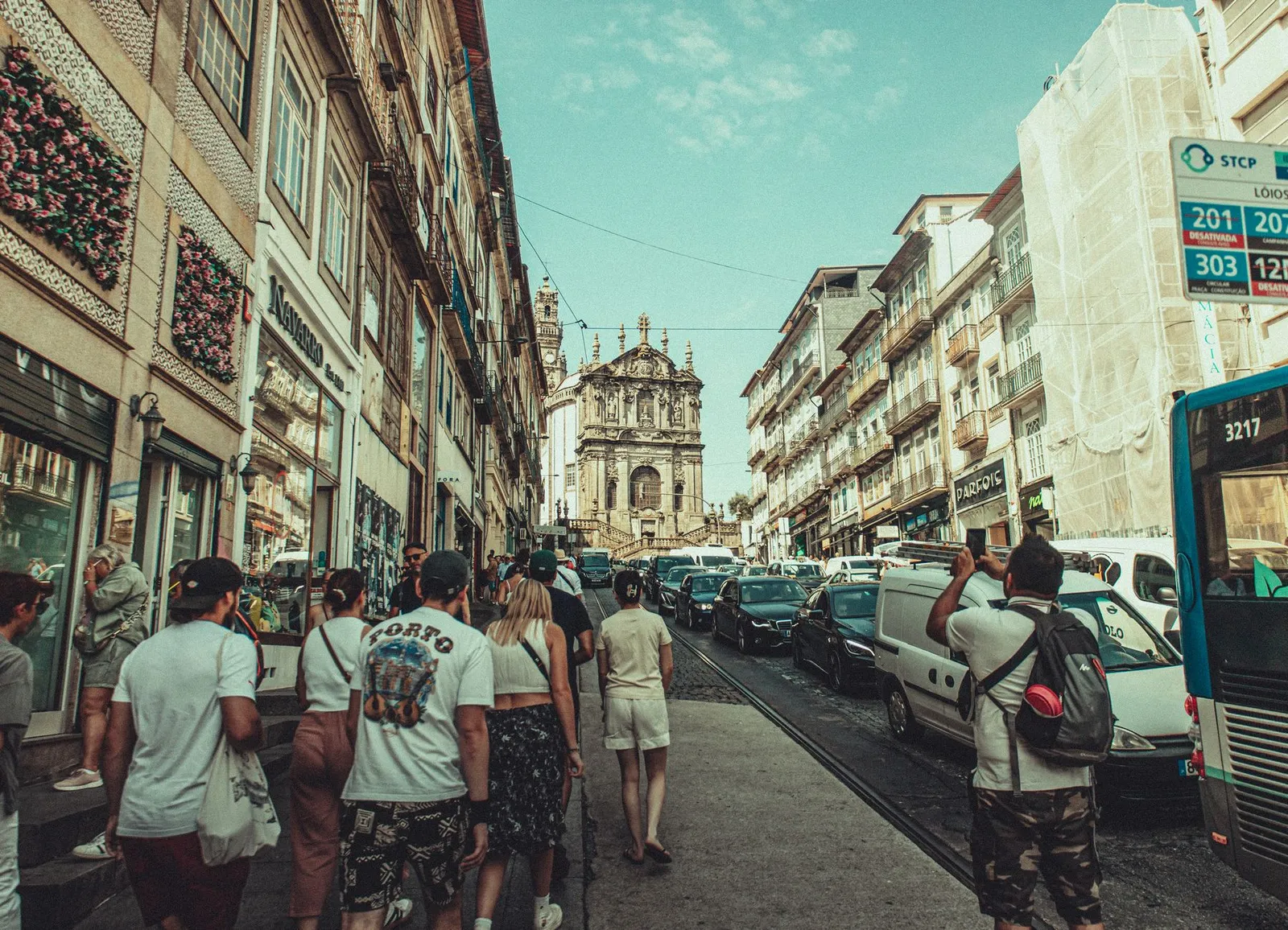 A bustling street in Porto filled with tourists and classic architecture under a clear blue sky.