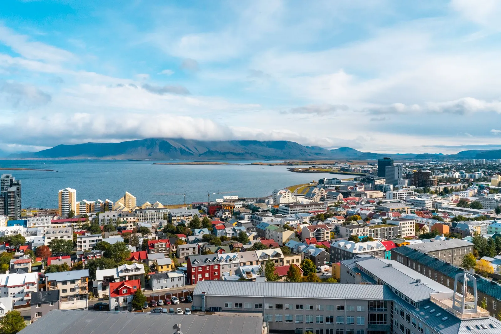 Aerial view of Reykjavik, Iceland featuring colorful buildings and ocean vistas under a partly cloudy sky.