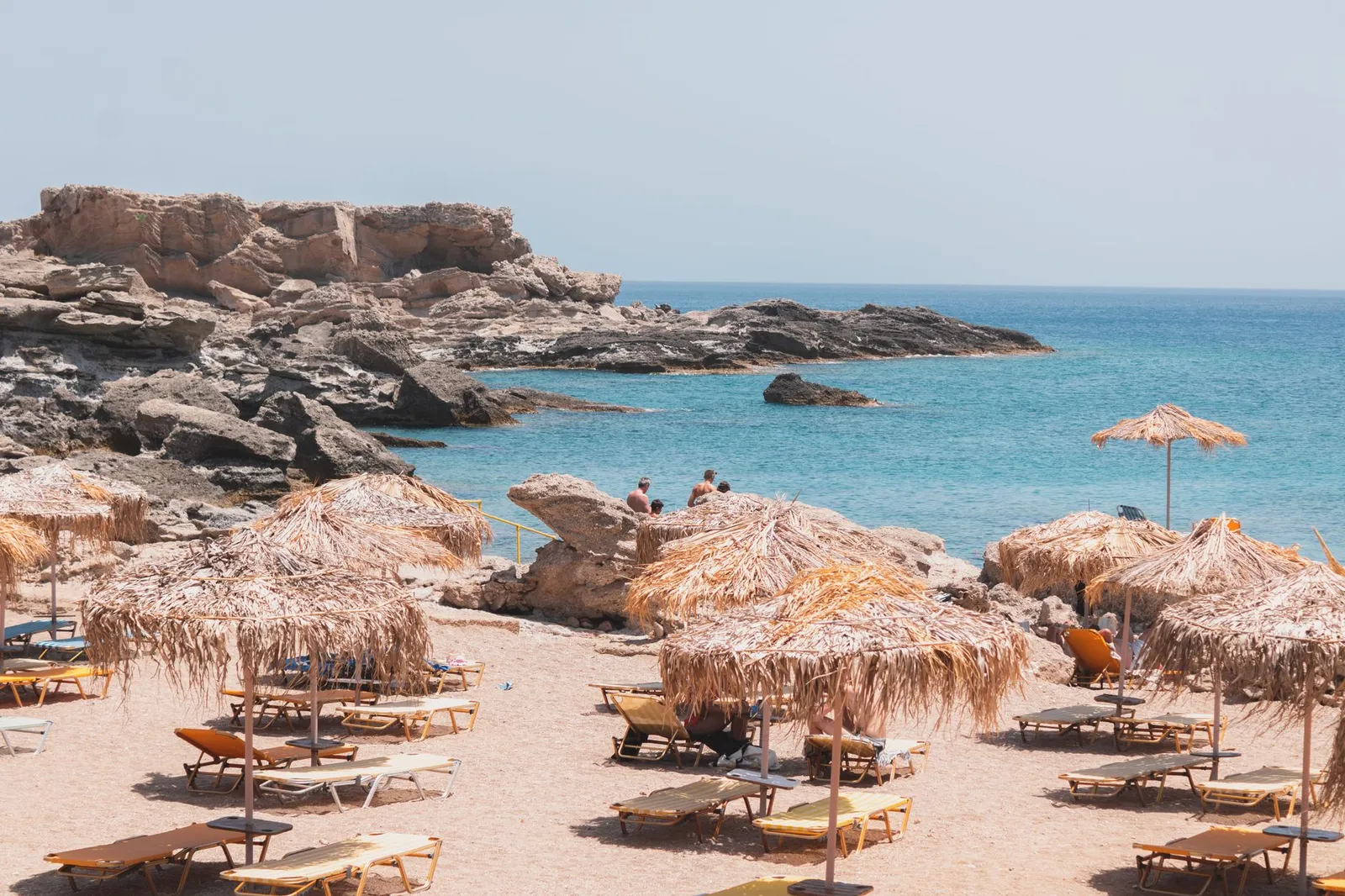 A scenic beach in Kallithea, Greece, featuring straw umbrellas and rocky formations by the sea.