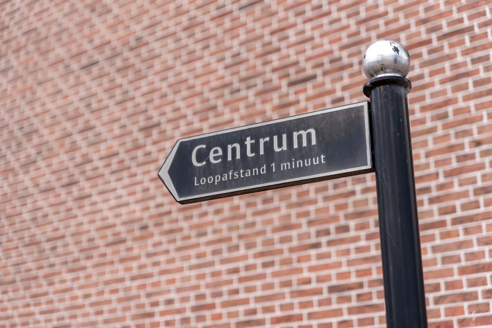 A directional sign to the city center reading 'Centrum, Loopafstand 1 minuut' against a brick wall.
