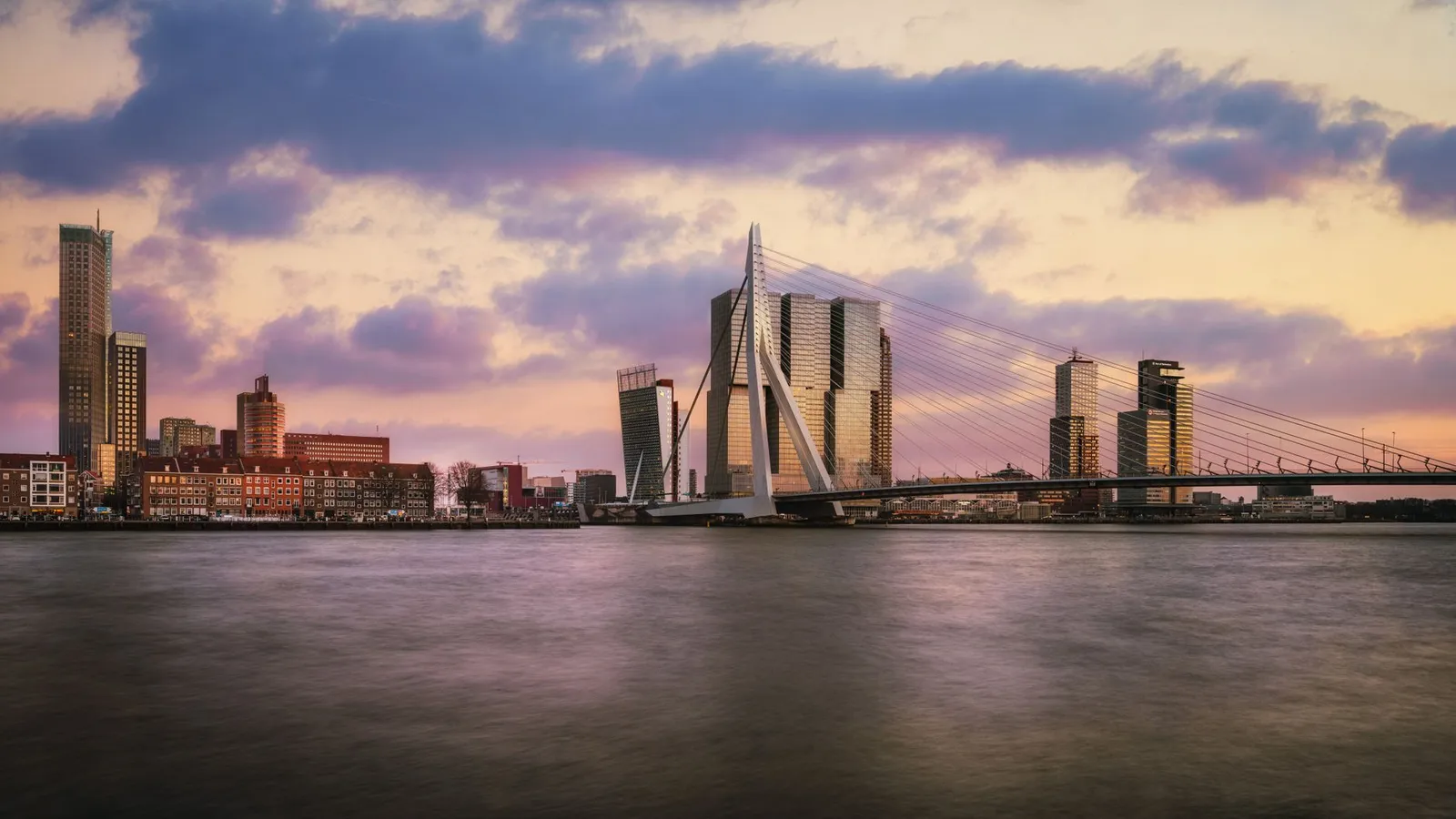 Captivating view of Rotterdam skyline and Erasmus Bridge during twilight over the Maas River.