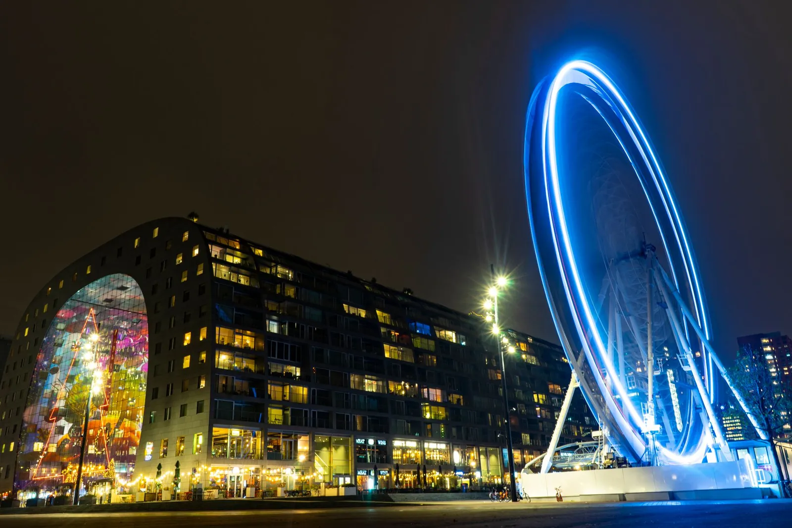 Long exposure of Rotterdam's Markthal and illuminated Ferris wheel at night.