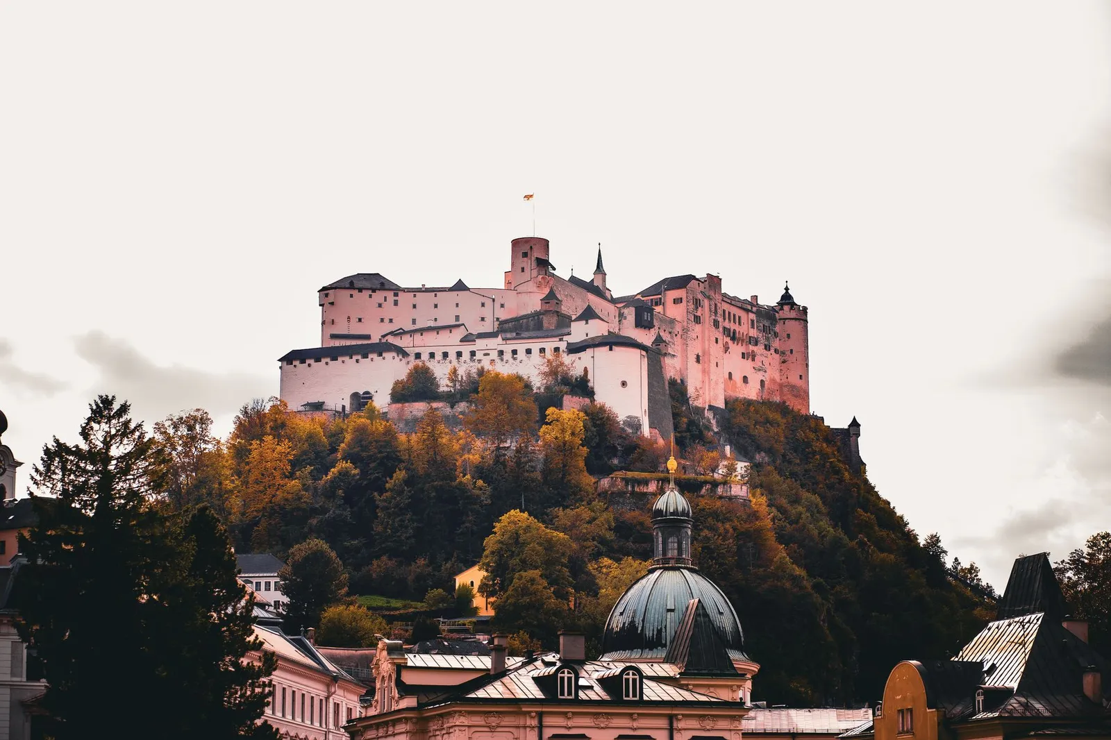 View of the Hohensalzburg Fortress atop a hill surrounded by vibrant autumn foliage in Salzburg, Austria.
