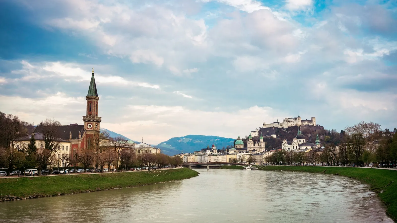 Picturesque Salzburg featuring Hohensalzburg Castle and Salzach River under a cloudy sky.