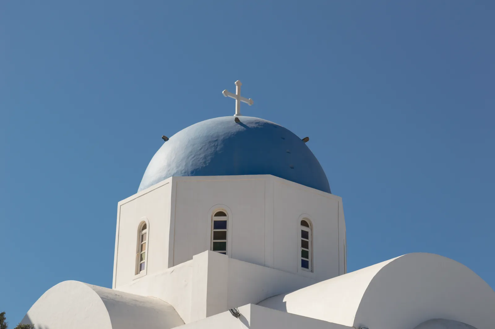 Orthodox church in Santorini with iconic blue dome and cross against a clear blue sky.