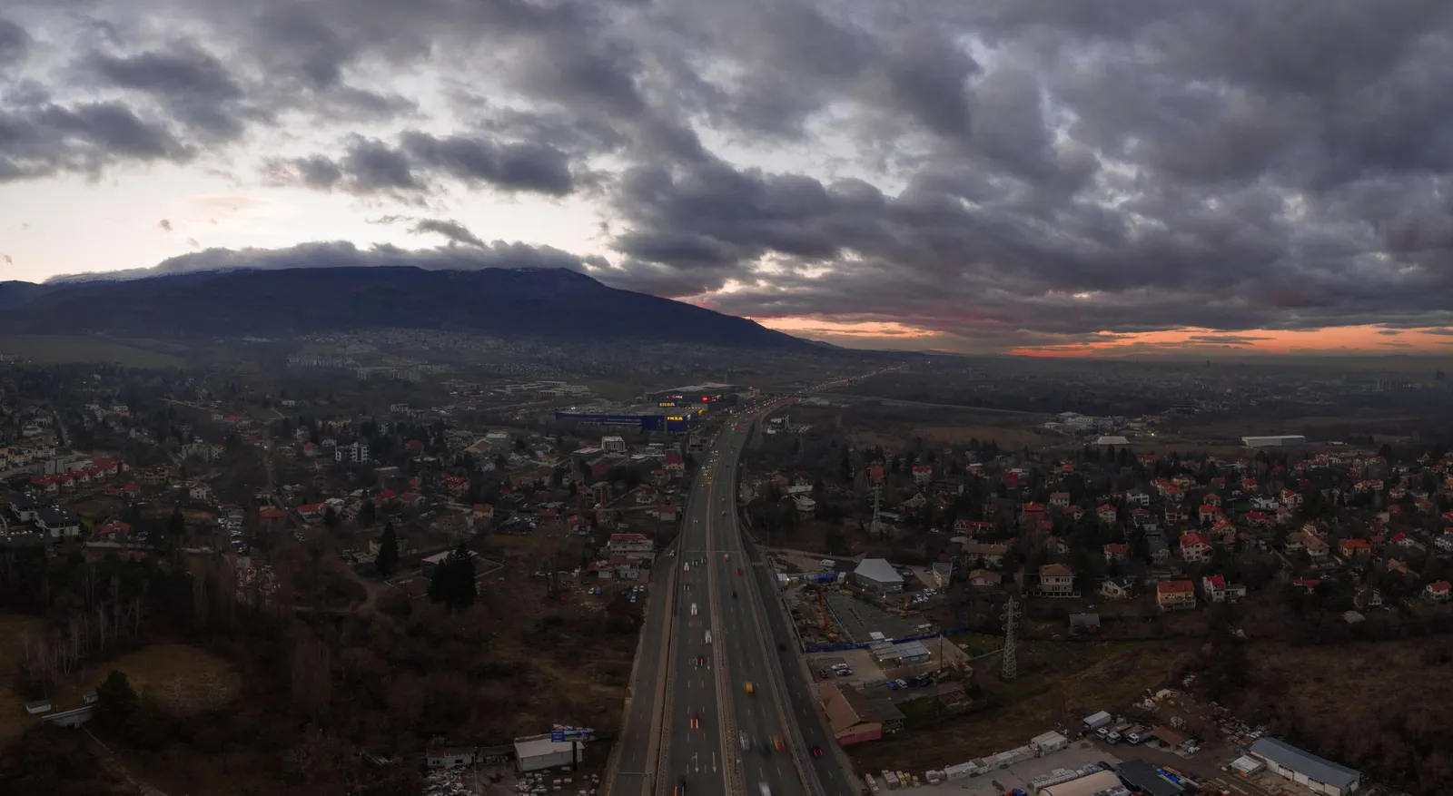 Aerial photograph of Sofia, Bulgaria with a highway, cityscape, and dramatic cloudy sky at sunset.
