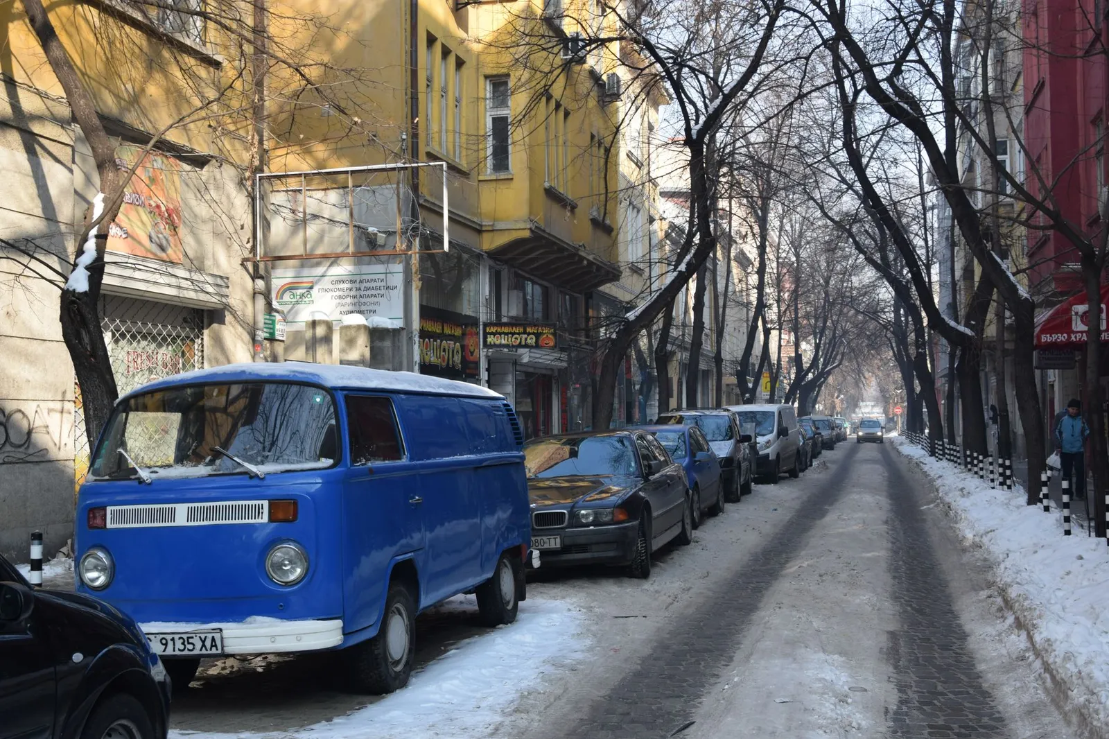 Urban street scene in Sofia with parked cars and snow-covered road in winter.