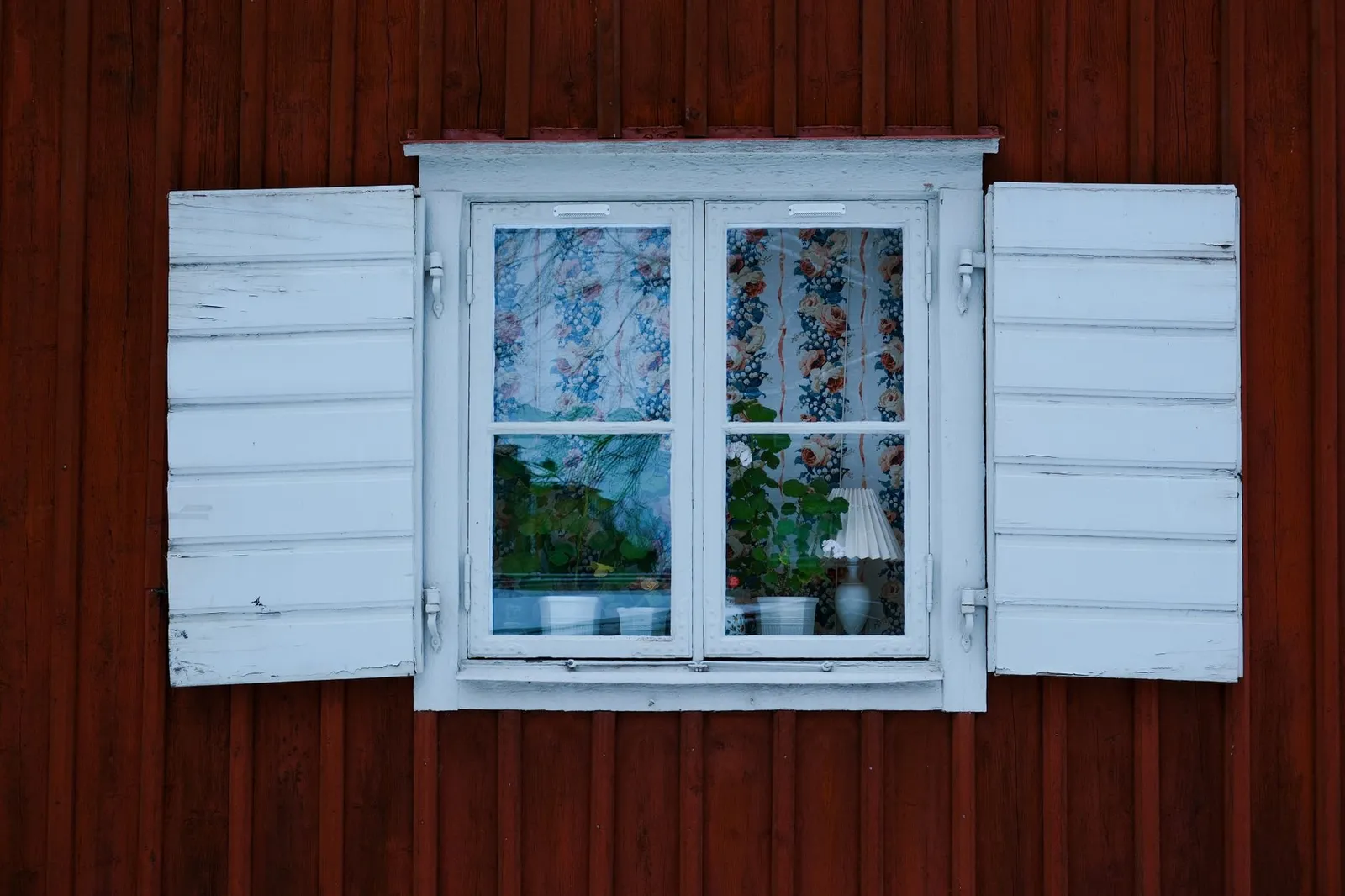 Close-up of a traditional Swedish window with white shutters and floral curtains in Södermalm, Stockholm.