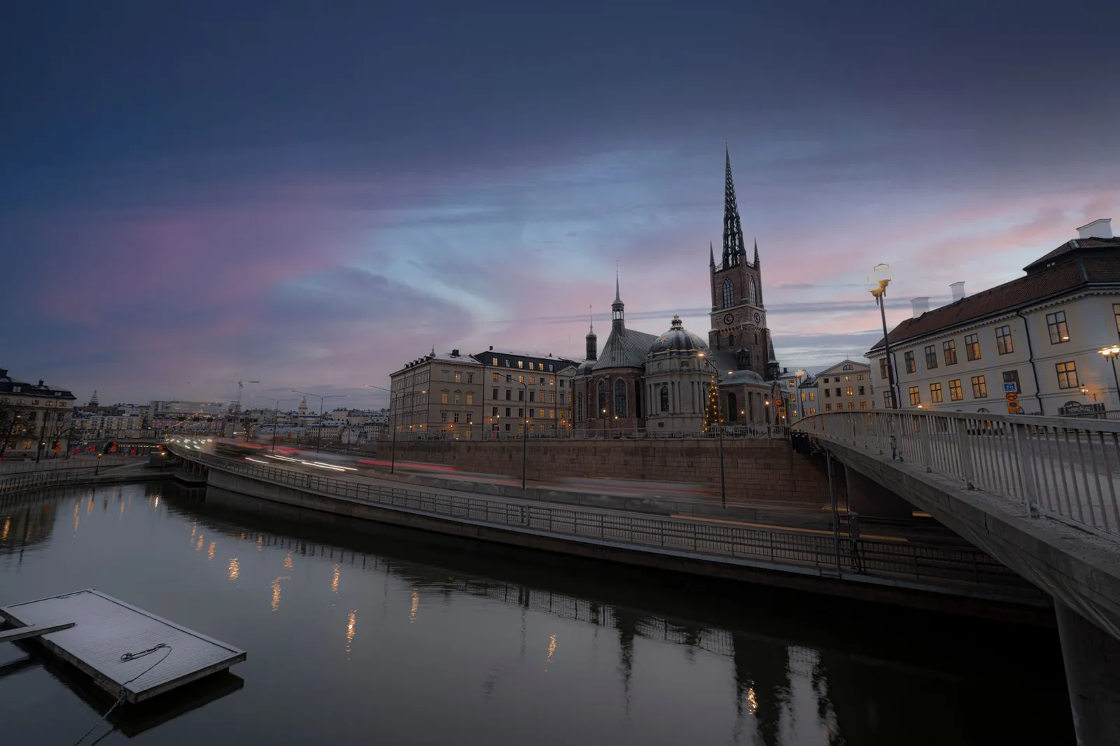 Twilight view of Riddarholmen Church and surrounding architecture in Stockholm, reflecting in calm waters.