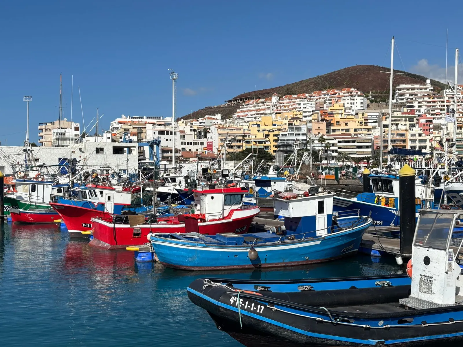 Vibrant fishing boats moored at Tenerife harbor against a backdrop of colorful hillside buildings.