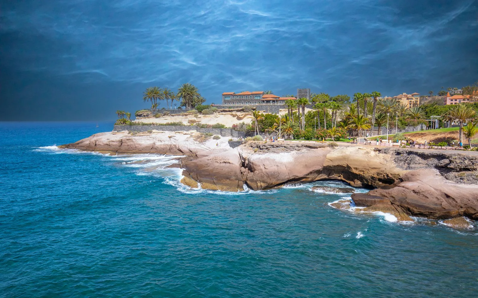 Breathtaking coastal view of Tenerife with palm trees and rugged cliffs under a vivid sky.