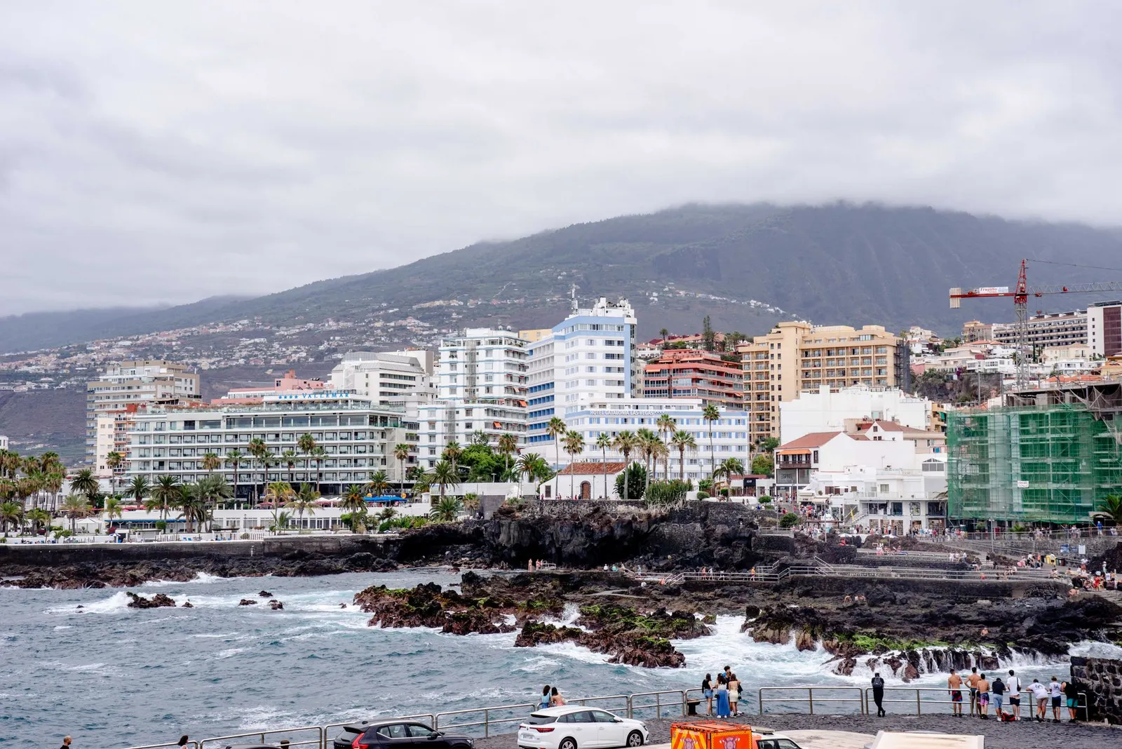 Seaside cityscape of Puerto de la Cruz, Tenerife, featuring hotels, rocky shore, and cloudy sky.