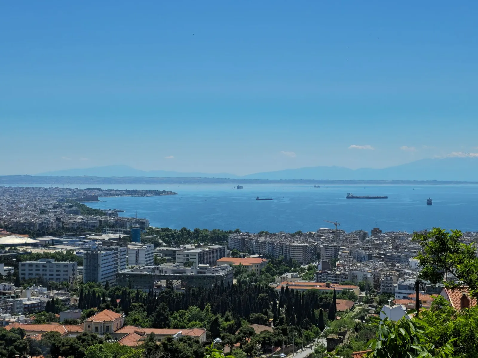A stunning aerial view of Thessaloniki cityscape with the harbor and distant mountains under a clear blue sky.
