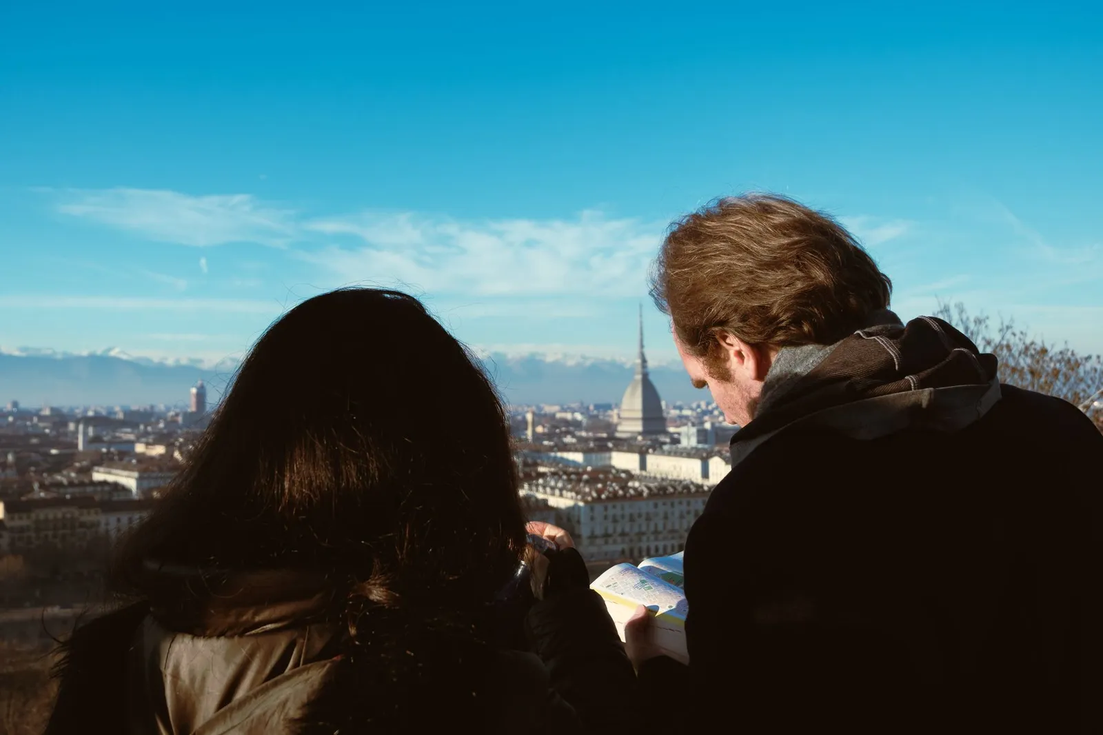 Traveling couple examines map with view of Turin and Mole Antonelliana in the background.