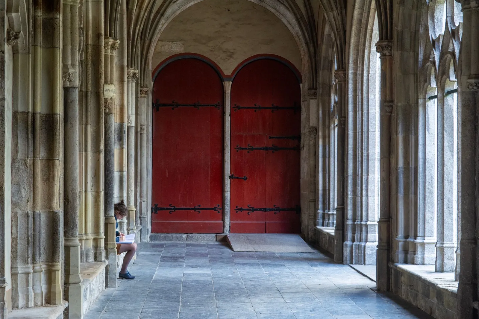 A serene Gothic cloister scene in Utrecht featuring red doors and ancient stone arches.