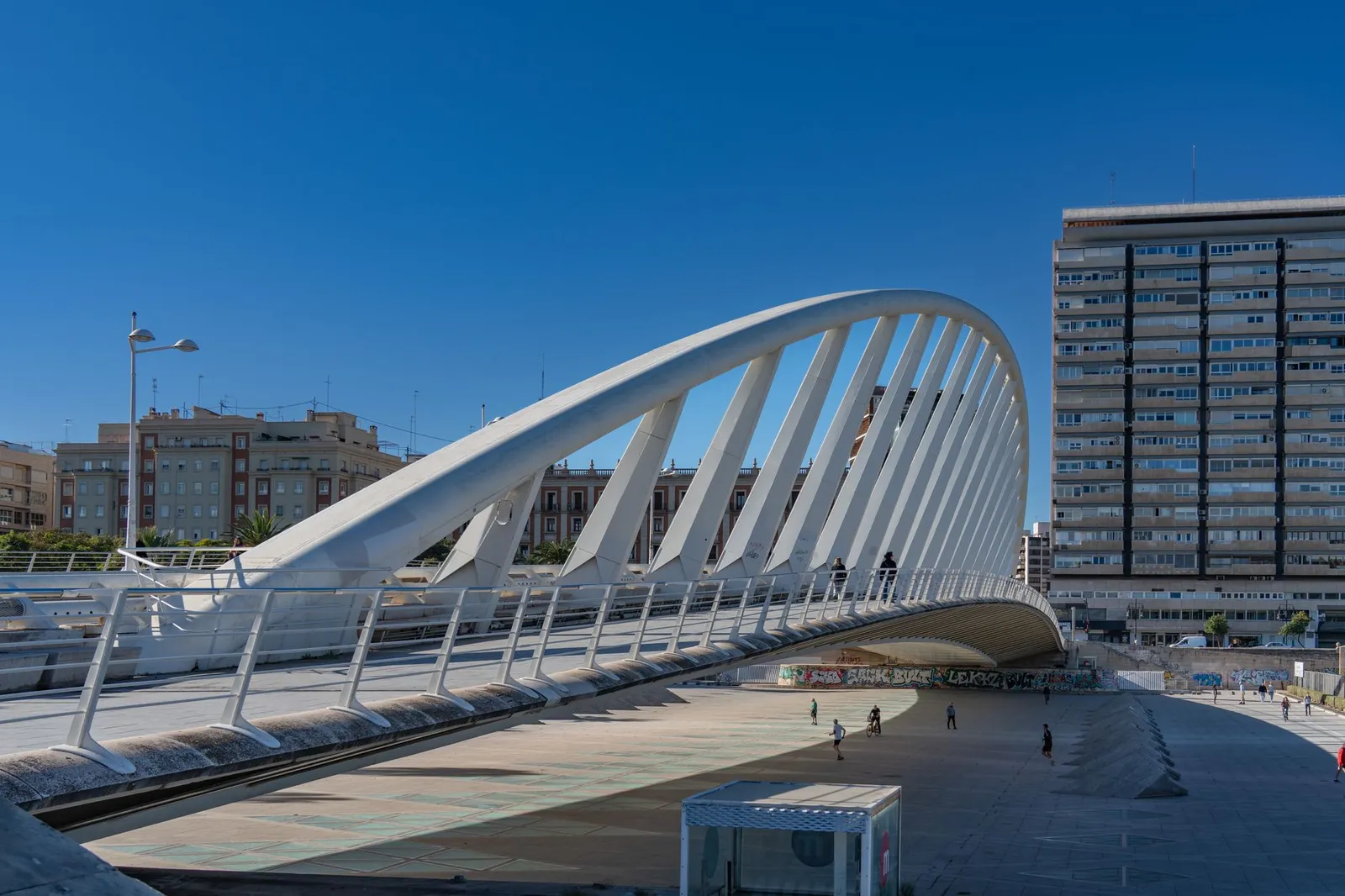 Contemporary white bridge in Valencia, Spain, with urban backdrop and vibrant blue sky.