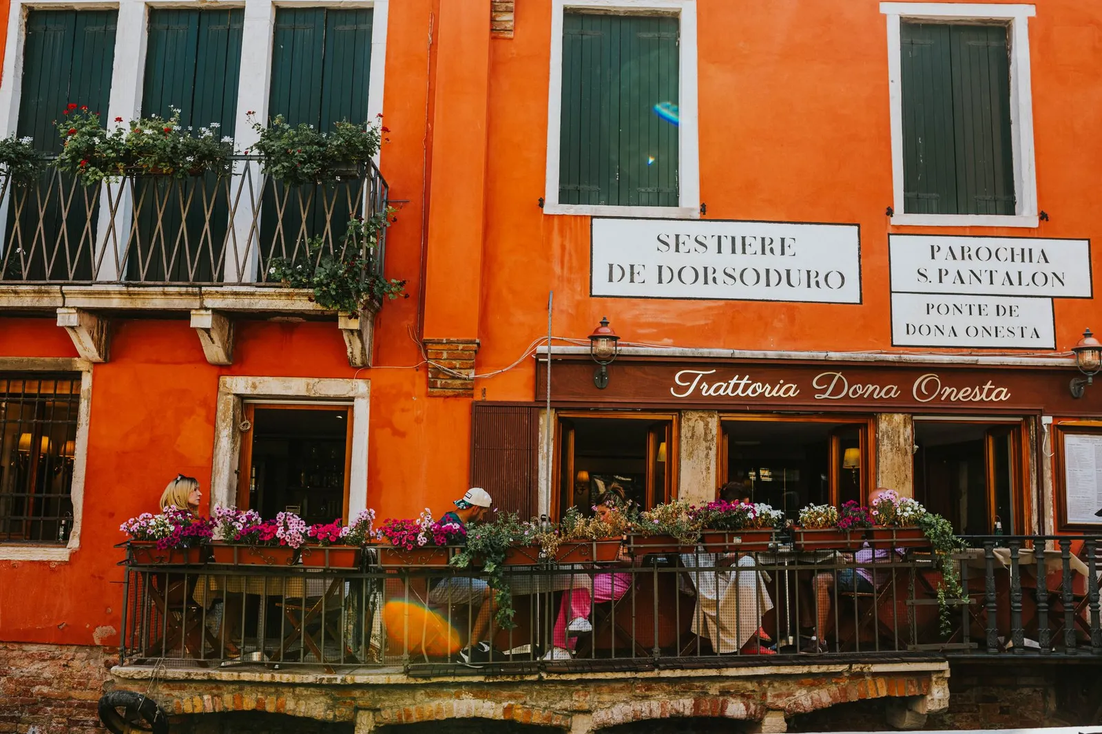 Quaint trattoria in Dorsoduro, Venice with outdoor seating on a vibrant orange facade balcony.