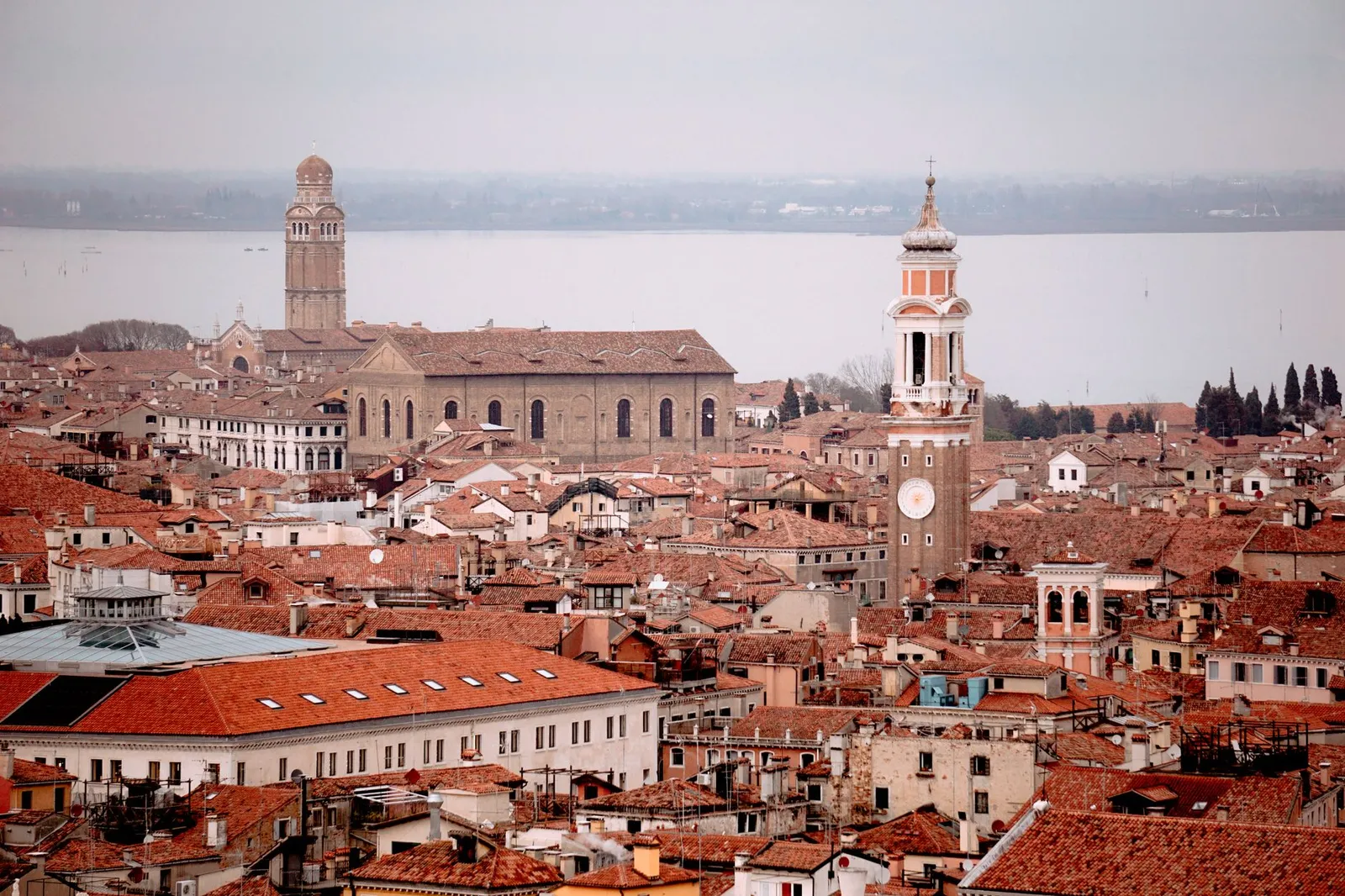 Panoramic aerial view of Venice showcasing red rooftops, towers, and historic architecture under a cloudy sky.