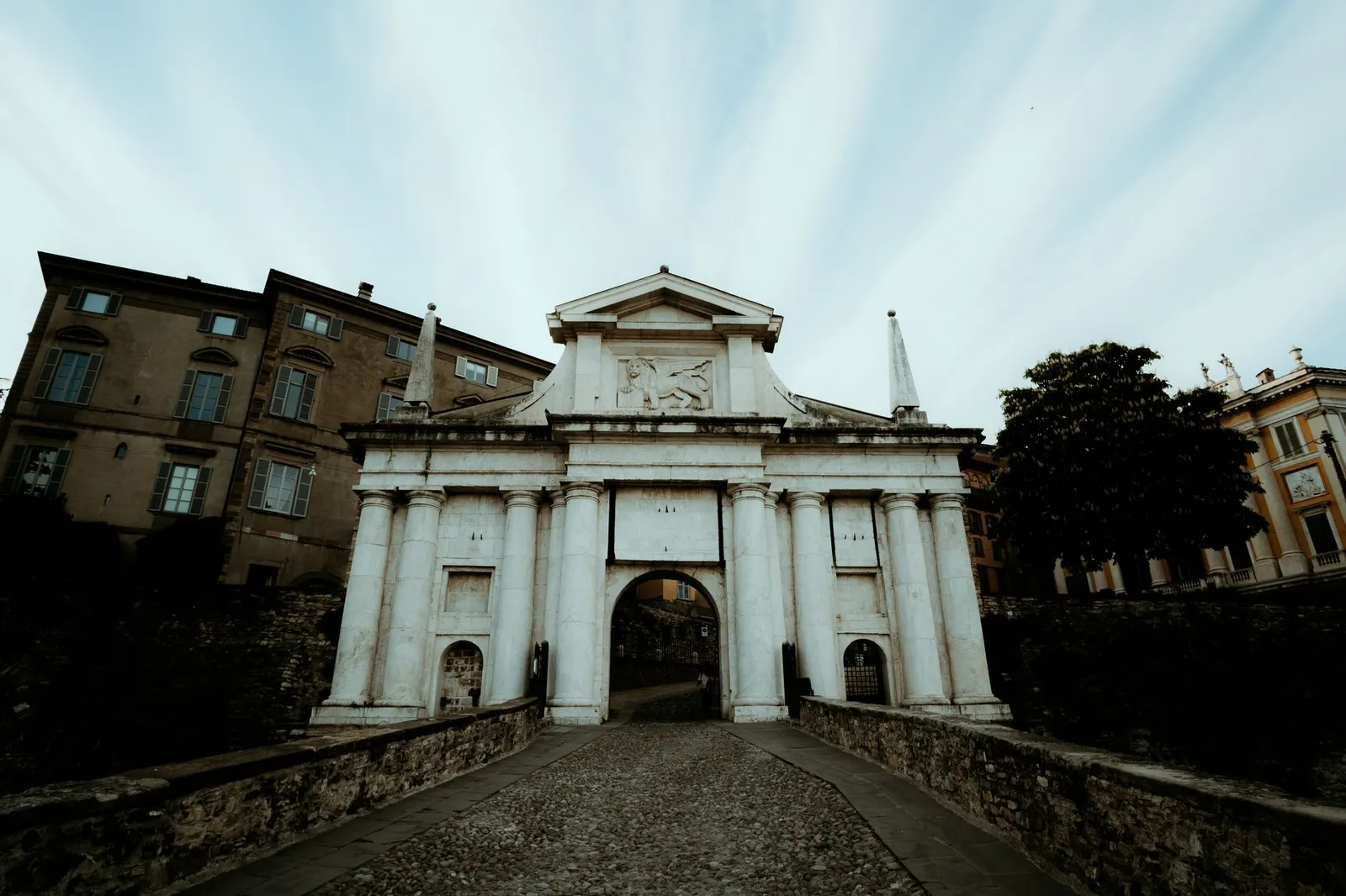 View of the iconic Porta San Giacomo in Bergamo, Italy against a dramatic sky.
