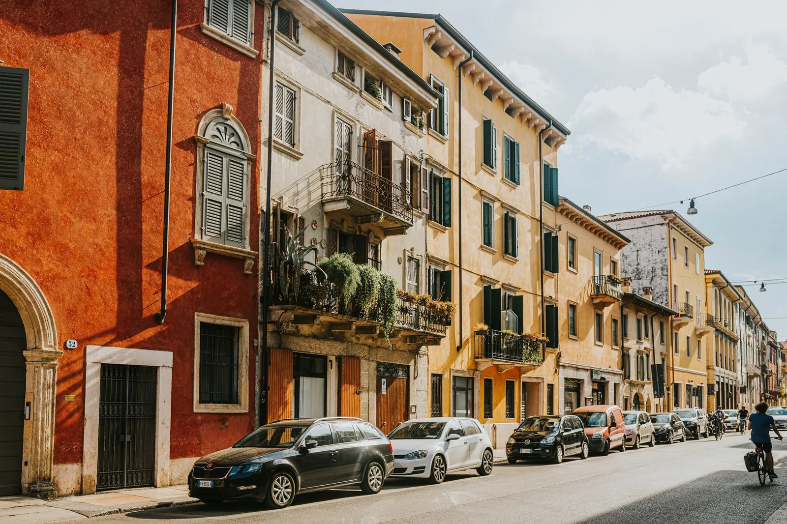 Colorful historic buildings and parked cars line the sunny streets of Verona, Italy.