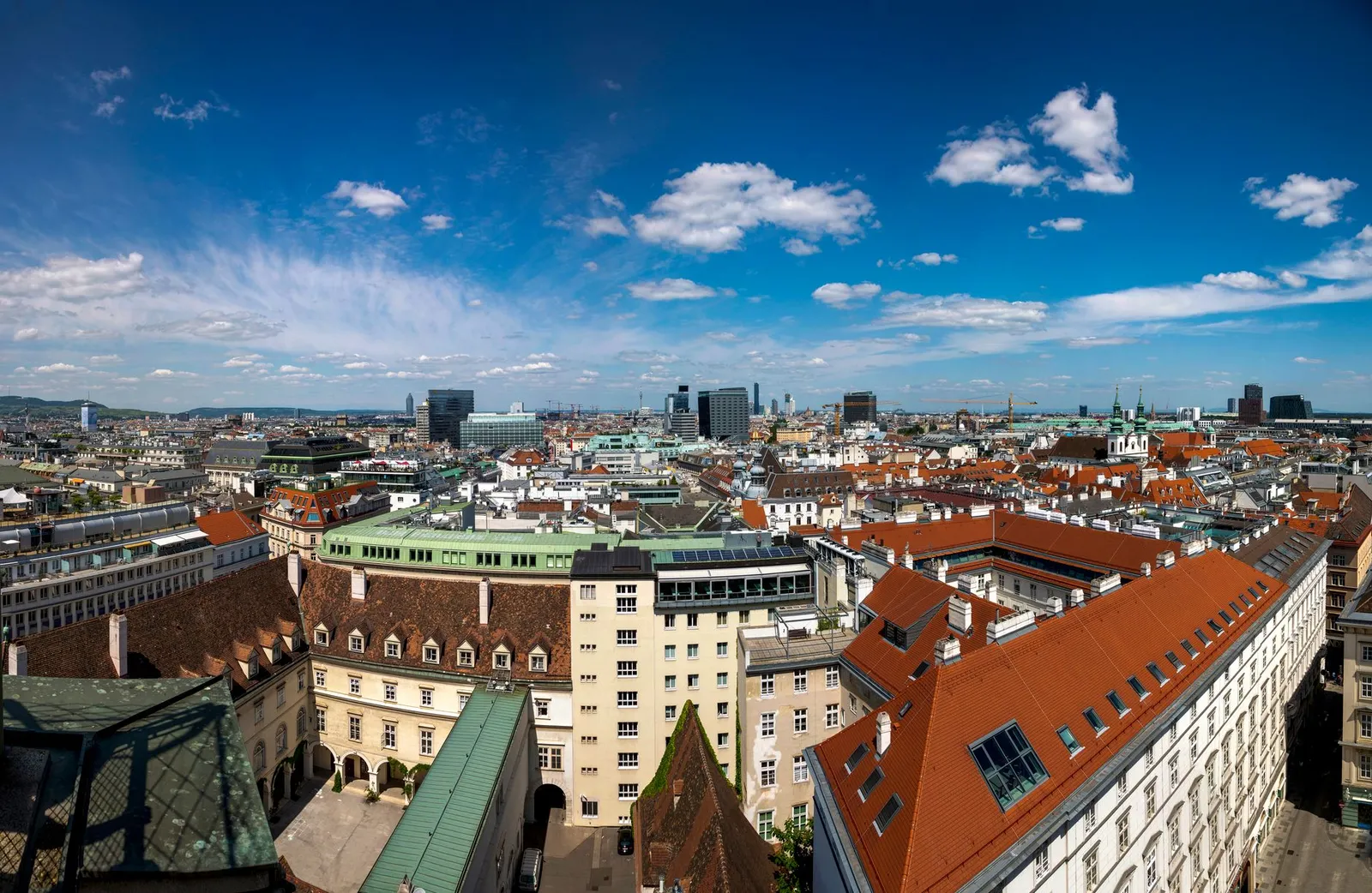 Wide-angle view of Vienna skyline featuring mix of historical and modern architecture under a bright blue sky.