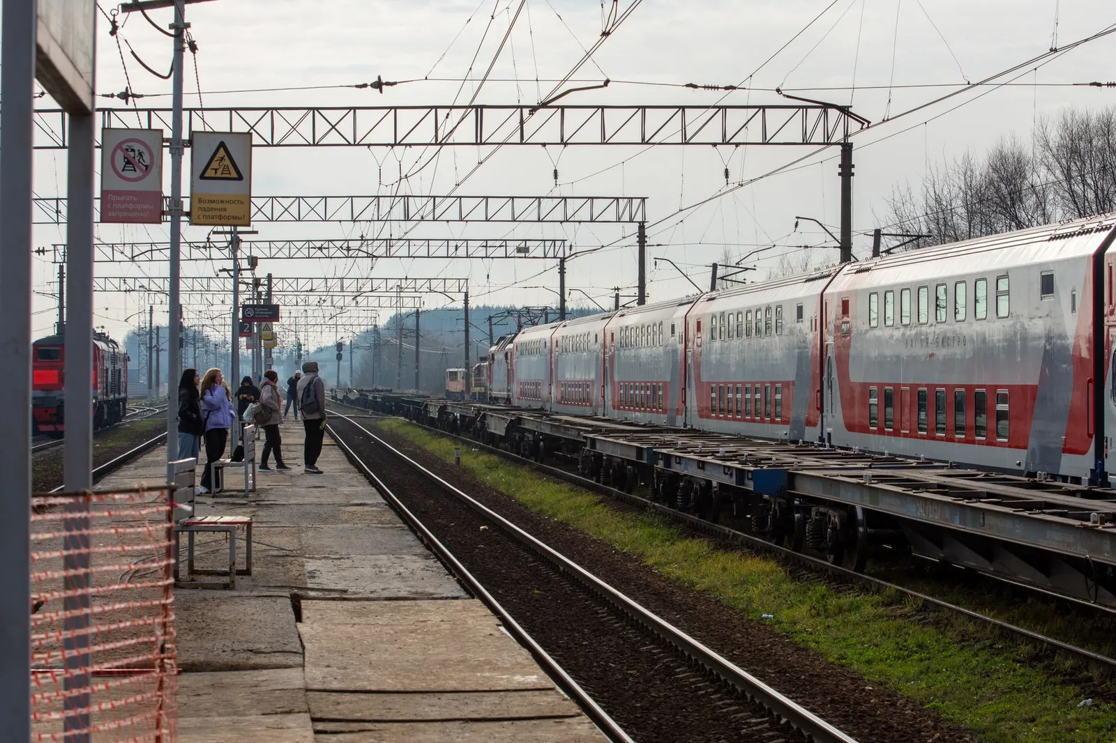 Passengers waiting on a railway platform beside a modern train during the day.