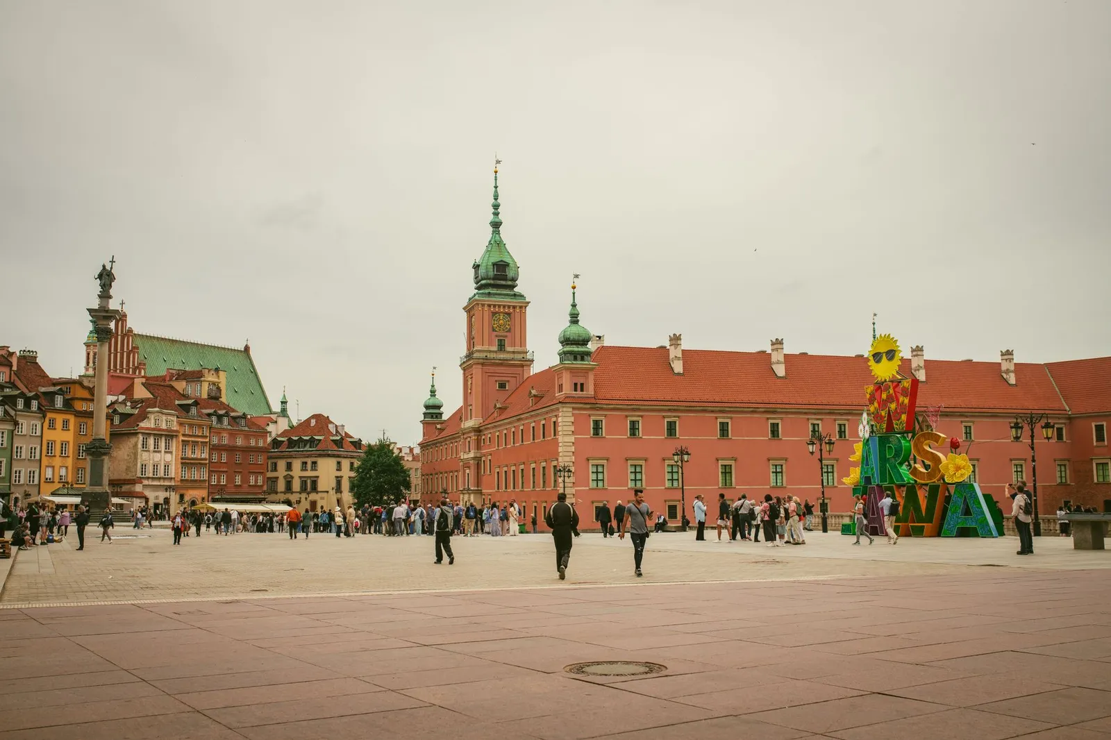 A bustling scene at Warsaw's Old Town Square featuring the Royal Castle and colorful buildings.