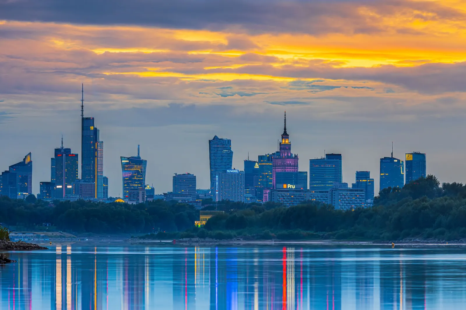 Experience the vibrant Warsaw skyline at sunset, reflecting beautifully in the river.