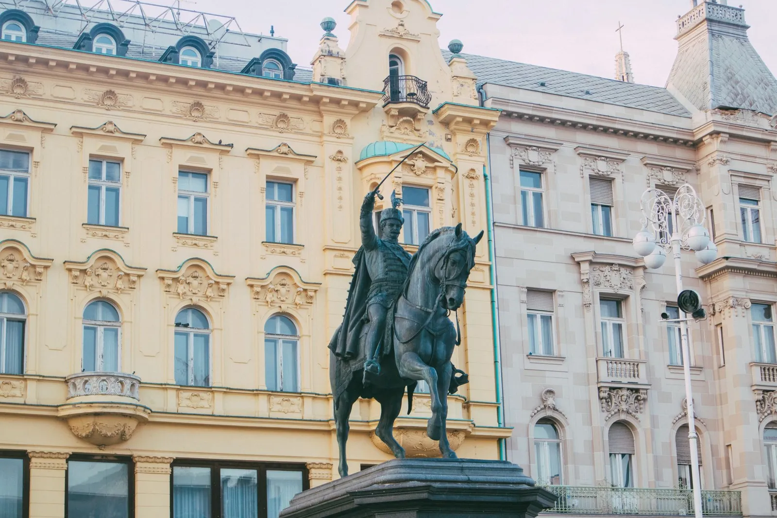 Historic equestrian statue in front of yellow and ornate townhouses in urban area.