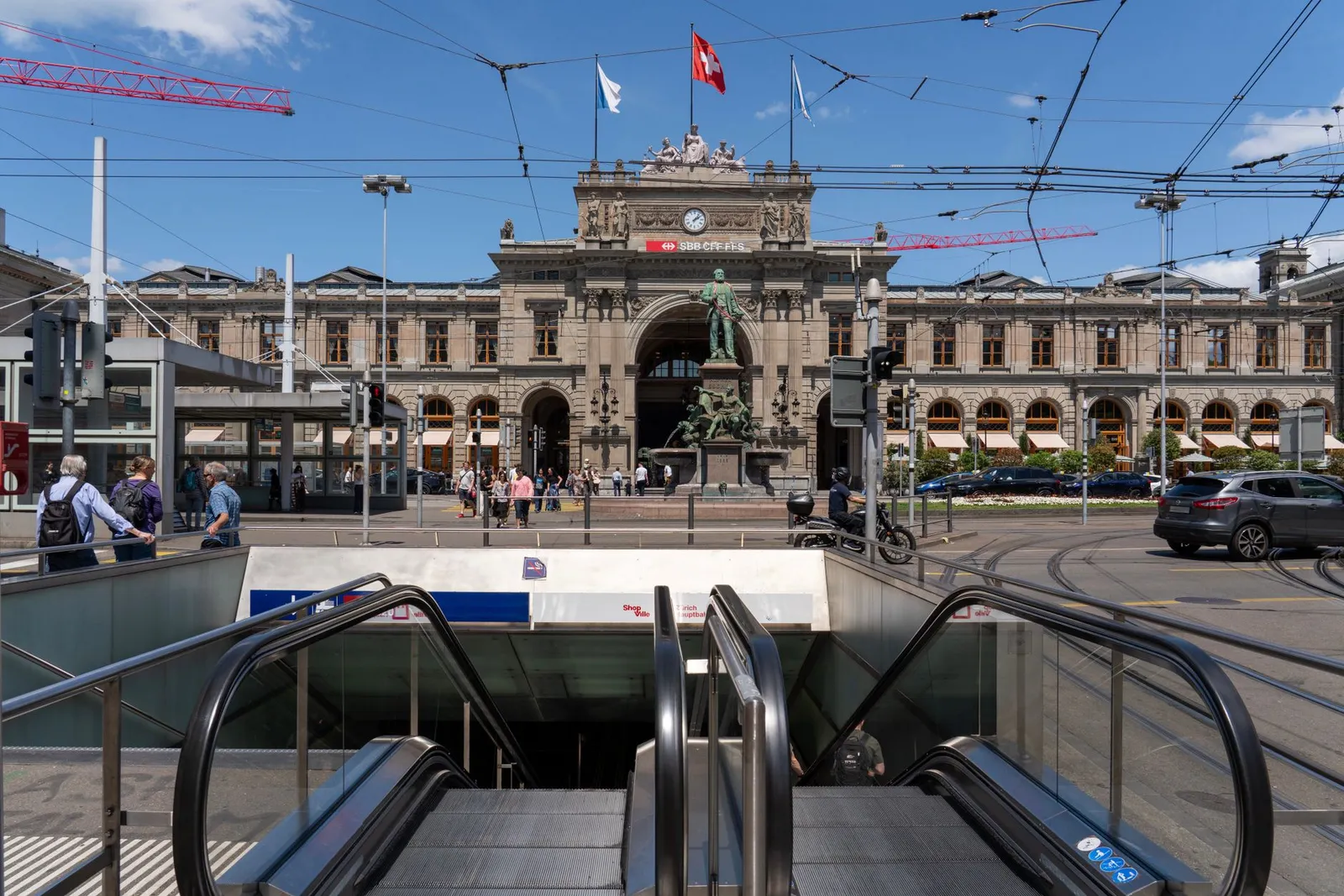 View of Zurich Hauptbahnhof facade with people and cars under a clear blue sky.
